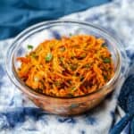 Raw carrot salad with shredded carrots and herbs on a blue background.