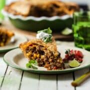 A slice of savory ground beef empanada pie with pie crust served with sour cream and cilantro.