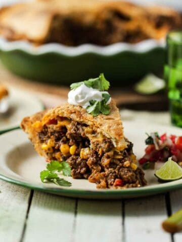 A slice of savory ground beef empanada pie with pie crust served with sour cream and cilantro.