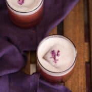 Frothy egg white cocktail recipe made with lilac syrup served with an edible lilac garnish.
