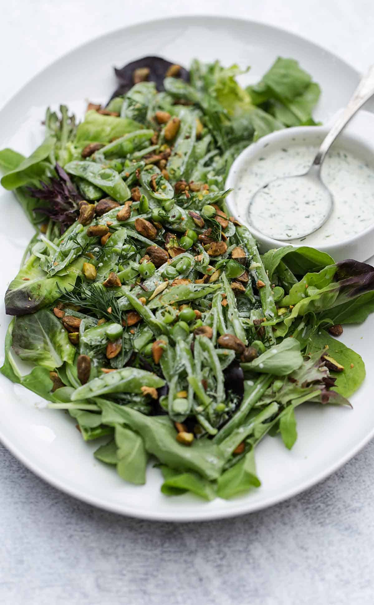 Salad with pistachios served on a white platter with extra dressing on the side